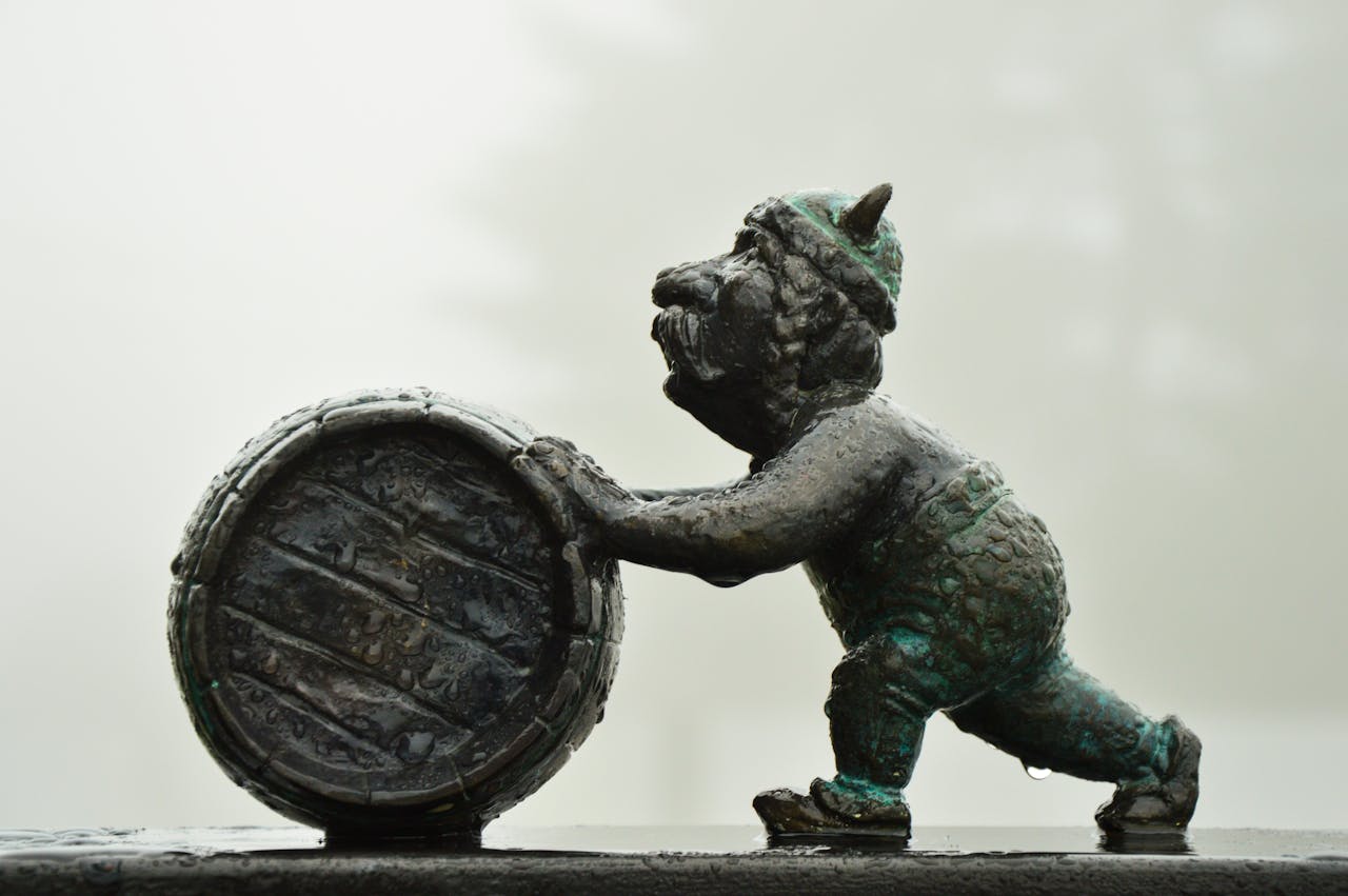 Close-up of a bronze gnome figurine pushing a barrel. Art sculpture with detail.