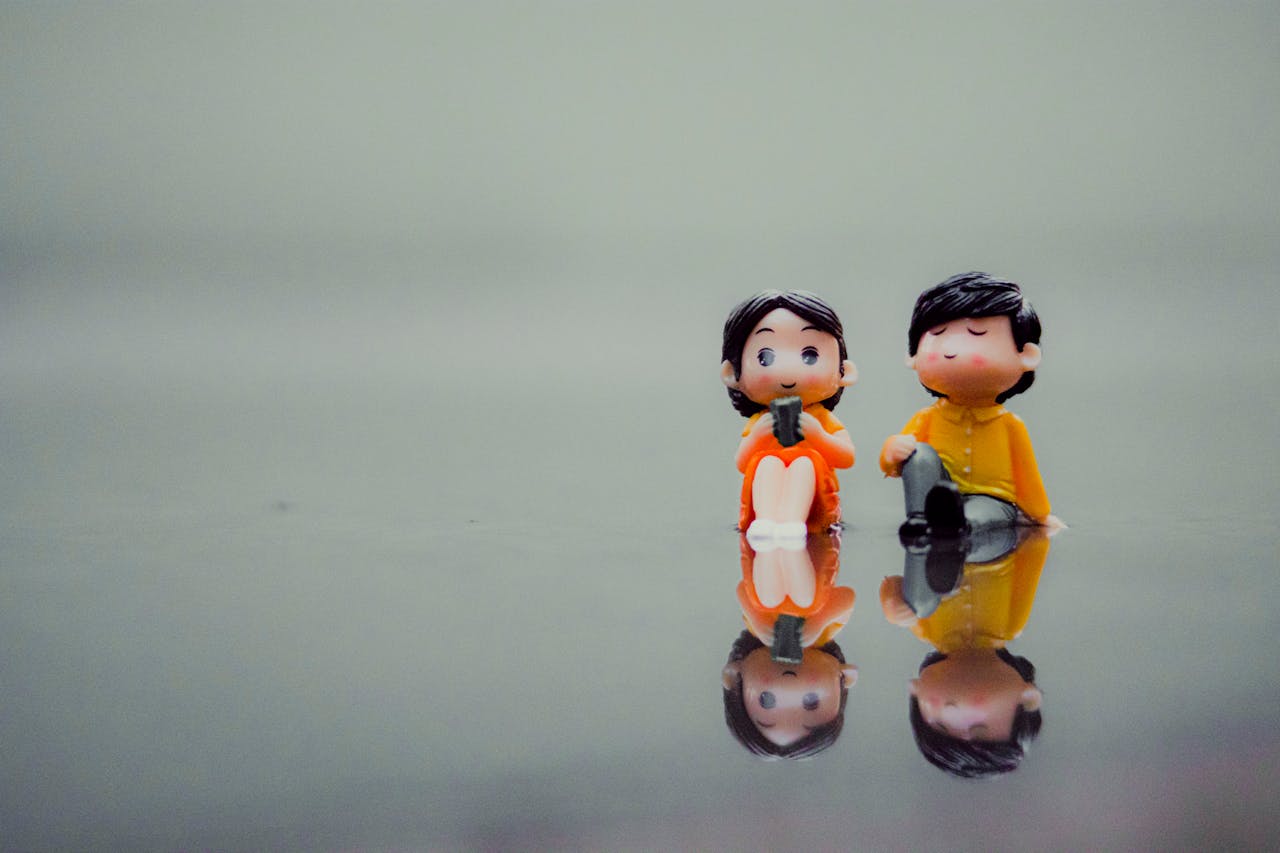 Two miniature figurines reflect on a smooth surface symbolizing love and creativity.